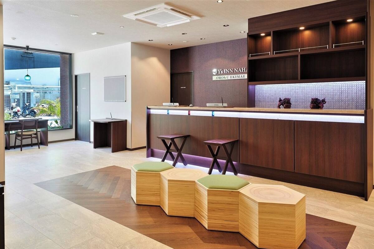 Un área de recepción moderna con mostrador de madera, taburetes de bar y vistas a la ciudad a través de amplios ventanales.