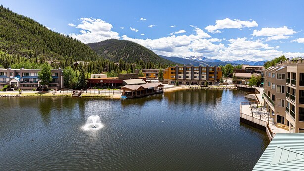 A lakeside view with buildings, a dock, and mountains in the background. - Lakeside Condo w/ Mountain & Lake Views from Balcony, Steps to Shops/Dining! (Keystone)