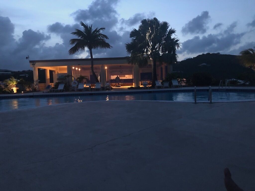 A resort with a pool, palm trees, and a building with outdoor seating.