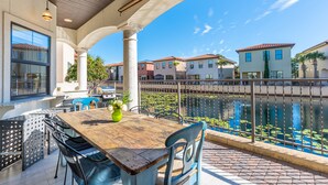Une terrasse avec une table et des chaises en bois, un vase vert et une vue sur un canal, avec des maisons en arrière-plan.