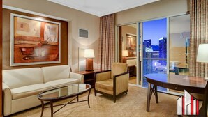 A hotel room with a sofa, armchair, and a glass table. There is a painting on the wall and a view of the cityscape through the window. - Vegas Condo w/ F1 Track & Strip Views, Jacuzzi (Las Vegas)