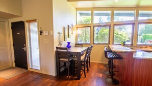 A dining area with a wooden table and chairs, a bar counter, and large windows with blinds. - Sparkling Clean Mid Century Modern Home in Ferry Street Bridge Area (Eugene)