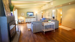 A modern living room with a fireplace, a grey sectional sofa, a small side table, and a television mounted on the wall. - Sparkling Clean Mid Century Modern Home in Ferry Street Bridge Area (Eugene)