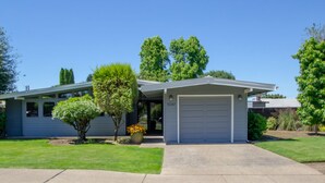 A modern two-story house with a garage, a well-maintained lawn, and mature trees. - Sparkling Clean Mid Century Modern Home in Ferry Street Bridge Area (Eugene)