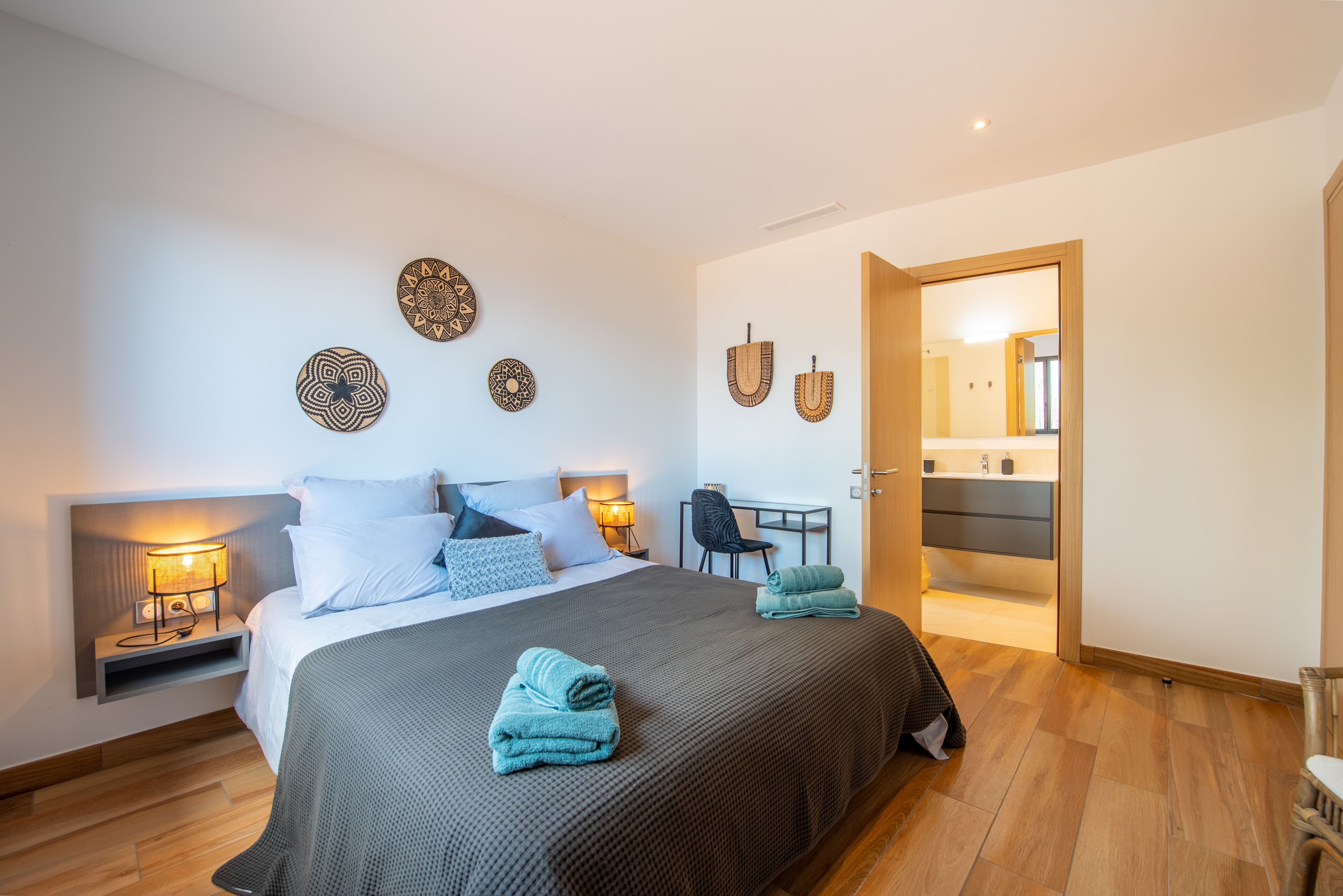 A modern hotel room with a large bed, bedside lamps, a desk, and a view into the bathroom.