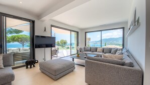 A modern living room with a large gray sectional sofa, a small ottoman, and a flat-screen TV mounted on the wall. - VILLA GIGARO SEA VIEW NEAR BEACHES (La Croix-Valmer)
