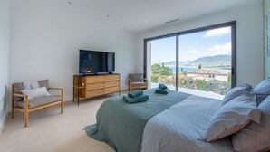 A modern bedroom with a large bed, a TV on a wooden dresser, and a view of a coastal landscape. - VILLA GIGARO SEA VIEW NEAR BEACHES (La Croix-Valmer)
