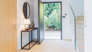 A modern hallway with a wooden door, a console table with a lamp, a mirror, and a glass door leading to a garden. - VILLA GIGARO SEA VIEW NEAR BEACHES (La Croix-Valmer)