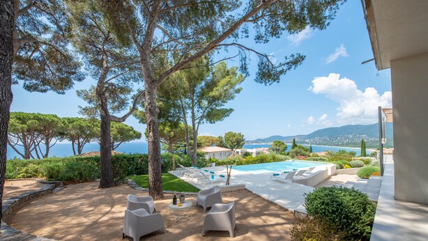 A poolside area with lounge chairs, a small table with a bottle, and a view of the sea and mountains. - VILLA GIGARO SEA VIEW NEAR BEACHES (La Croix-Valmer)