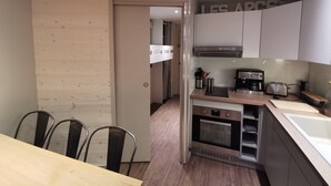 A modern kitchen with a built-in oven, a coffee maker, and a toaster. There is a wooden dining table with chairs. - Arcs 1800: Renovated 3BR 🏔️ 4 Crystals + Parking Incl. 🚗 - Transarc 100m (Bourg-Saint-Maurice)