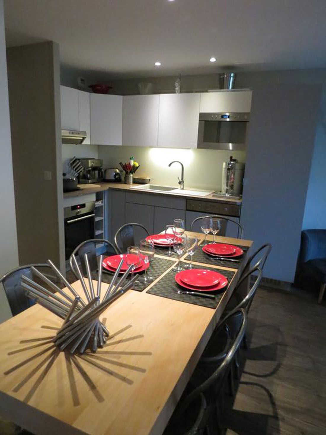 Una cocina moderna con armarios blancos, una campana extractora de acero inoxidable y un comedor con una mesa de madera dispuesta para cuatro.