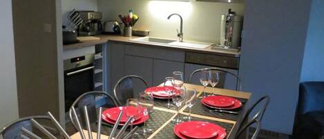 Una cocina moderna con armarios blancos, una campana extractora de acero inoxidable y un comedor con una mesa de madera dispuesta para cuatro.