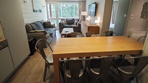 A modern living room with a wooden dining table and chairs, a sofa, and a TV mounted on the wall. - Arcs 1800: Renovated 3BR 🏔️ 4 Crystals + Parking Incl. 🚗 - Transarc 100m (Bourg-Saint-Maurice)