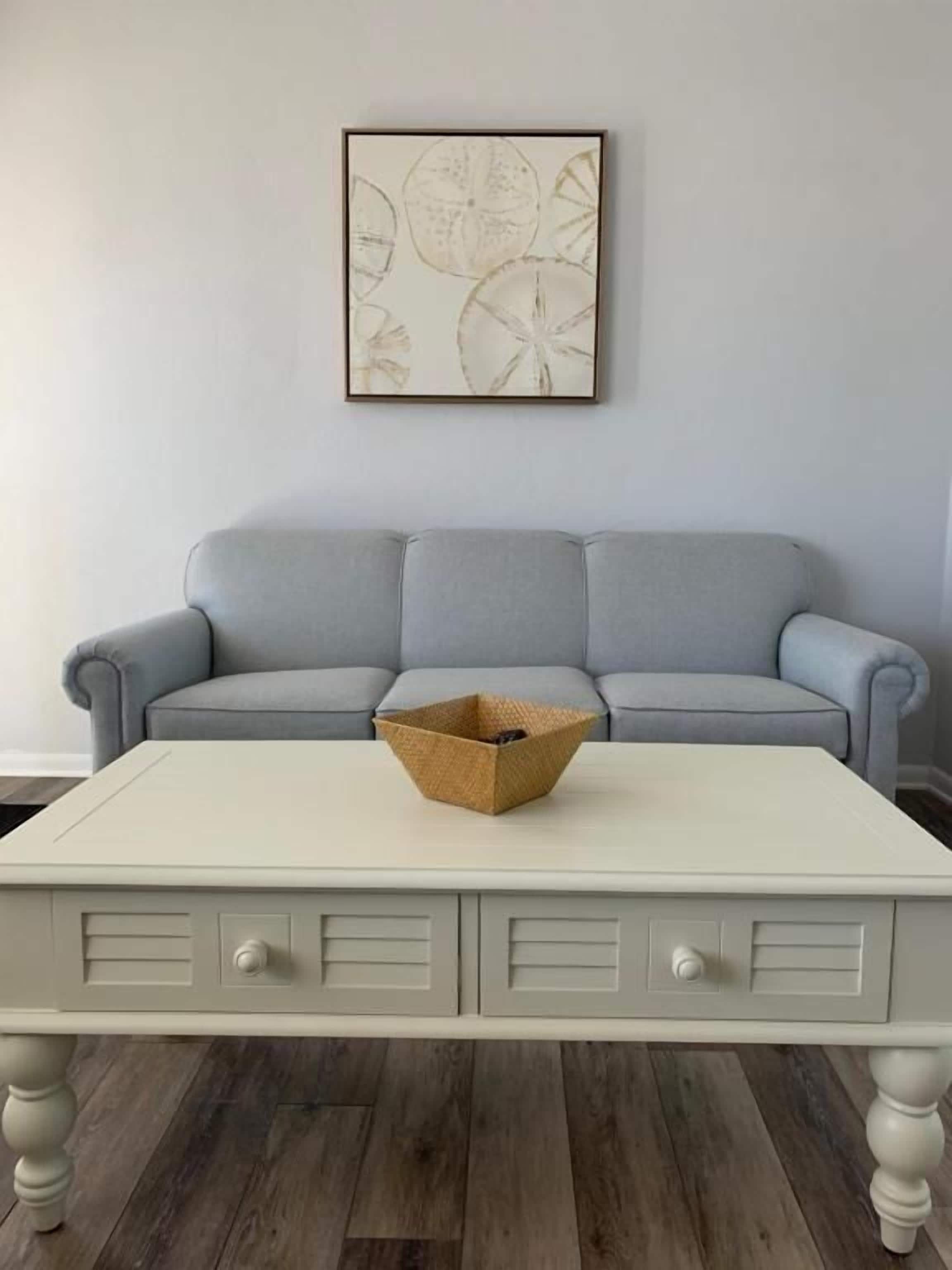 A white table with drawers and a woven basket on top, placed in front of a light blue sofa.