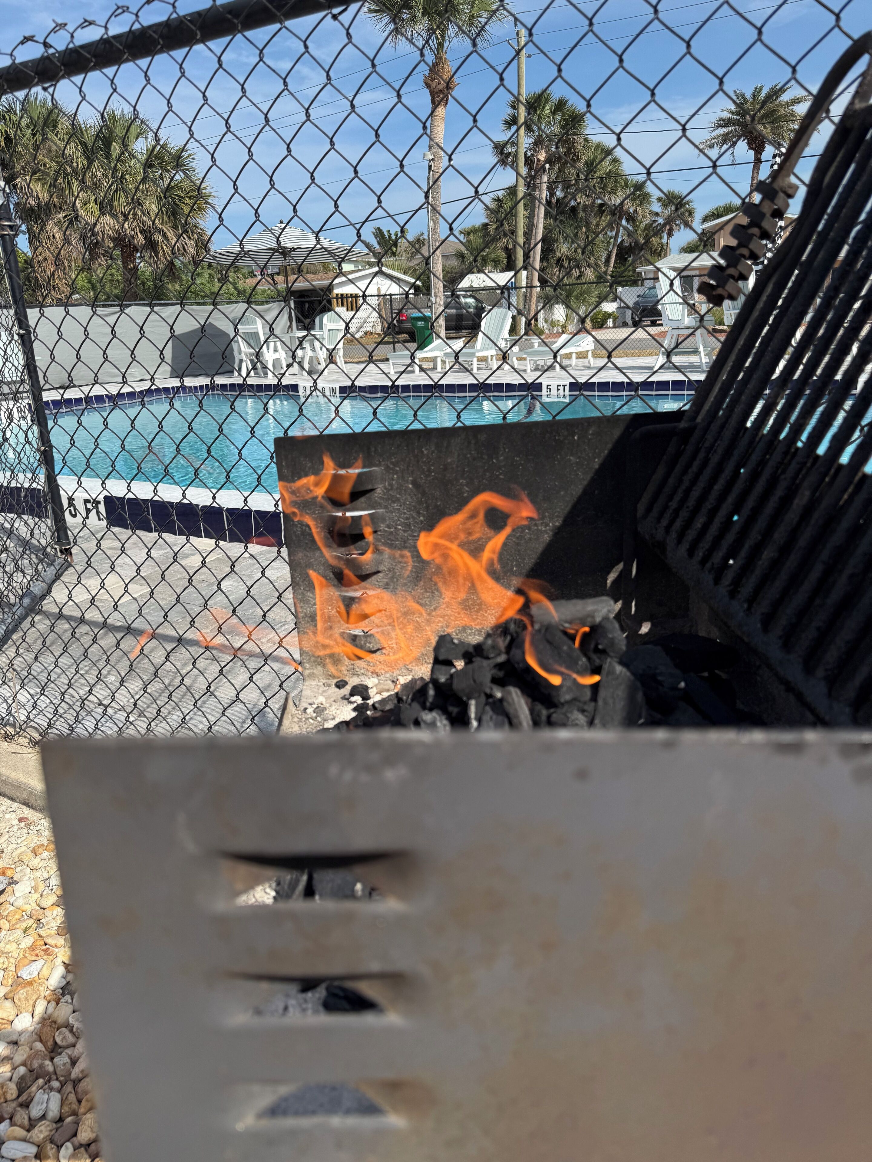 Ein stacheldrahtumzäunter Bereich mit Schwimmbecken, Grill und Holzkohlefeuer.