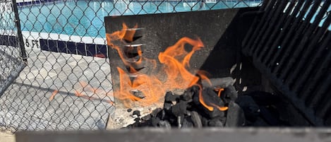 A chain-link fence enclosing a swimming pool area with a grill and charcoal fire.
