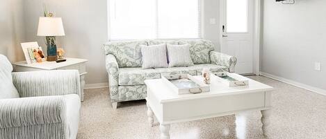 A living room with a white sofa, a patterned sofa, a white coffee table, and a side table with a lamp and decorative items.