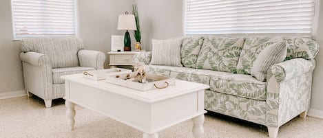 Un salon avec un canapé blanc, un fauteuil assorti, une table basse blanche et un canapé à motifs.