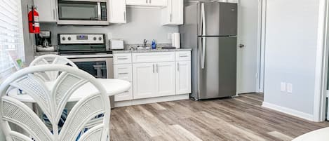 Une cuisine moderne avec des meubles blancs, des appareils en acier inoxydable, un coin repas blanc avec une chaise et un téléviseur à écran plat fixé au mur.