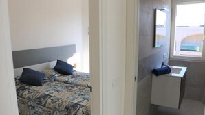 Un dormitorio con cama, almohadas y mesita de noche. Incluye un baño con lavabo y espejo.