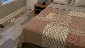 Une chambre à coucher avec un lit, une table de chevet, un vase de fleurs, une fenêtre avec des volets et un lustre.