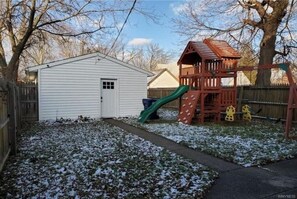 Backyard playhouse with a slide and adjacent shed, surrounded by a fence.