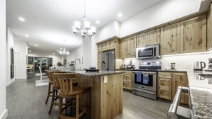 A modern kitchen with wooden cabinets, stainless steel appliances, and a central island with bar stools. - Luxurious Oregon Coast Townhouse with Mesmerizing Views! (Coos Bay)