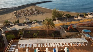 A beach resort with sun loungers, a pool, and a view of the sea.