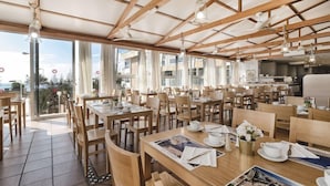A spacious dining area with wooden tables and chairs, large windows, and a high ceiling with exposed beams.