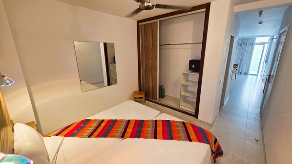 A bedroom with a bed, a ceiling fan, a mirror, a wardrobe, and a door leading to another room. - Hotel Europalace (San Bartolomé de Tirajana)