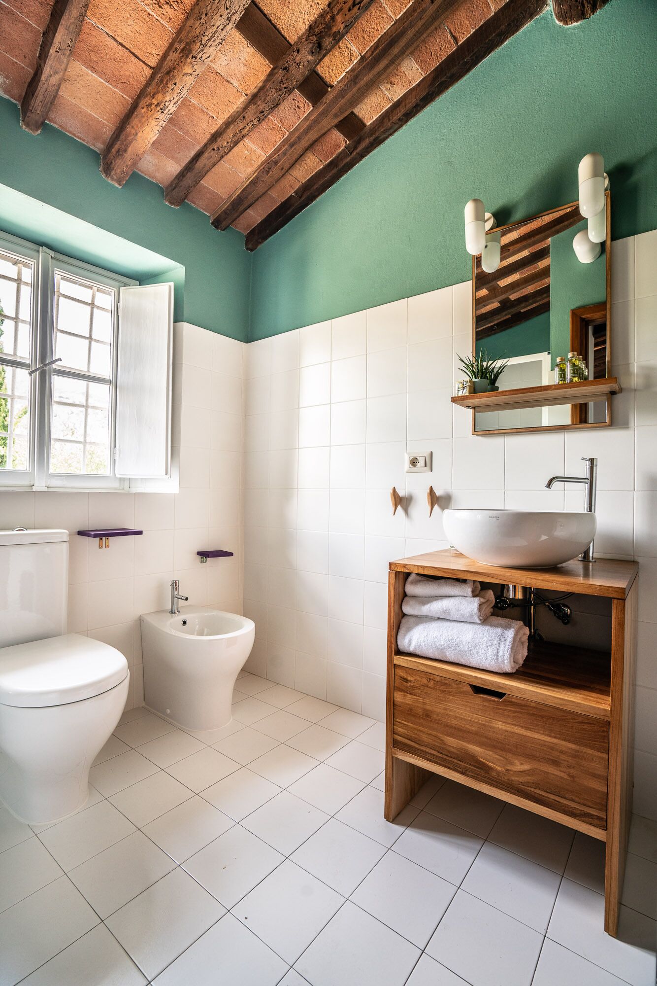 A bathroom with a toilet, bidet, and sink under a wooden beam ceiling.