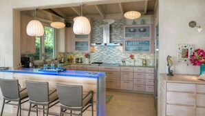 Una cocina con una isla central, taburetes de bar, iluminación colgante y un salpicadero con diseño de mosaico.