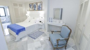 Un dormitorio con cama, mesita de noche, silla y un pequeño escritorio con espejo y un florero.