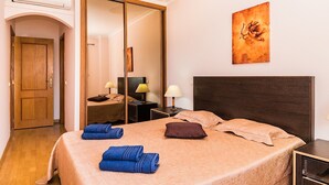 Quarto de hotel com cama, guarda-roupa, mesa de cabeceira, abajur e um quadro na parede.