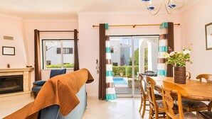 Uma sala de estar moderna com um sofá, uma mesa de jantar com cadeiras, uma lareira e vista para uma piscina através de uma porta de vidro.