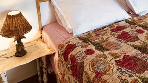 En seng med flettet sengegavl, en sengetlampe og et blomstret sengetæppe.