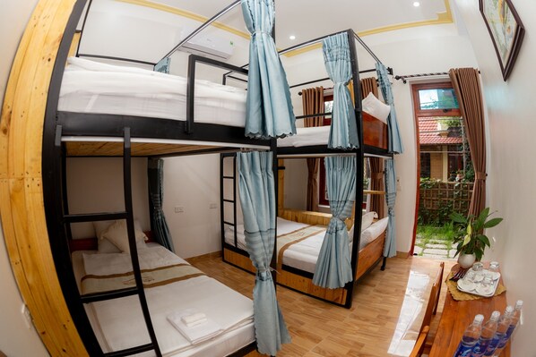 A bunk bed room with curtains, a wooden table with bottles, and a view of the outside.