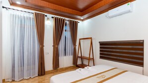 A hotel room with a bed, curtains, an air conditioner, and a wooden shelf.