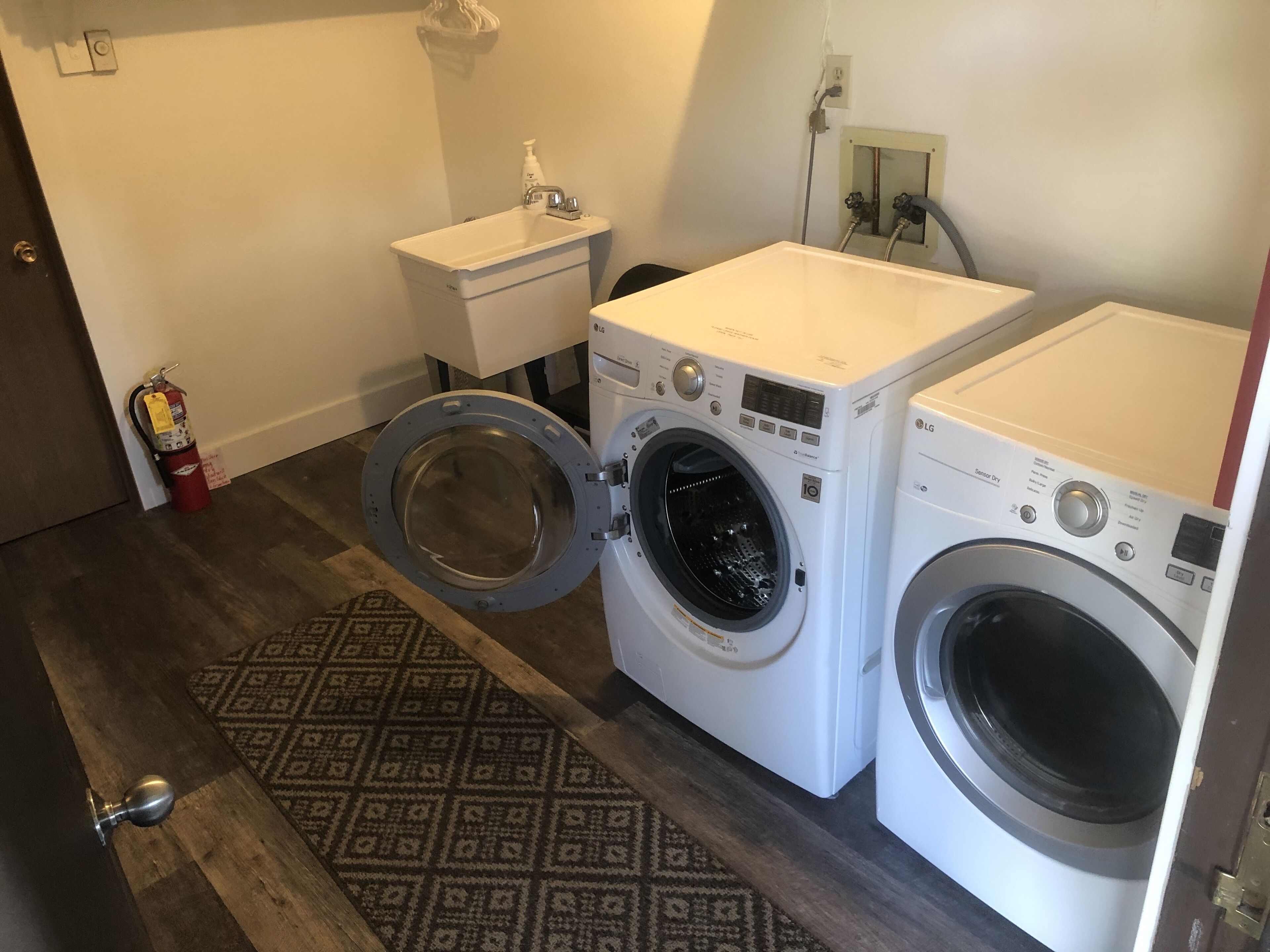A laundry room with two front-loading washing machines, a small sink, and a fire extinguisher.