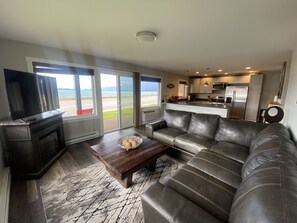 A modern living room with a leather sofa, a coffee table, and a flat-screen TV. The room has large windows offering a view of the outdoors. - Edgewater #1 Grizzly (Polson)