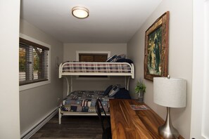 Ein kleines Zimmer mit einem Etagenbett, einem kleinen Tisch mit Lampe und einem gerahmten Bild an der Wand.