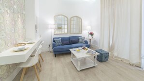 Una sala de estar con un sofá azul, una mesa de centro blanca y una pequeña mesita de noche con una lámpara.