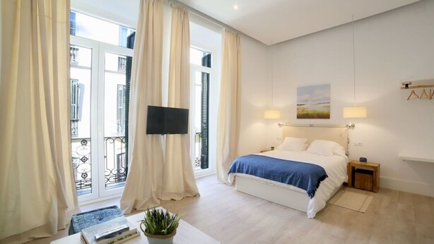 Un dormitorio con cama, mesitas de noche, televisor y ventana con cortinas.