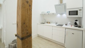 Una cocina compacta con armarios blancos, un microondas, una tetera y un lavabo.