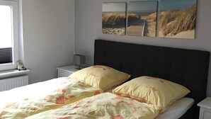 Ein Schlafzimmer mit einem Bett, zwei Nachttischen, einem Fenster und drei Bildern an der Wand.