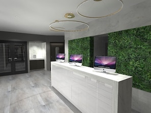 A reception area with a white reception desk, two monitors, and a green wall with plants.