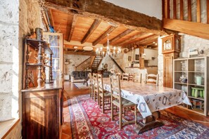 A rustic interior with a dining area, wooden beams, a chandelier, and a staircase leading to an upper level. - Homerez - House in Thenac (Thenac)