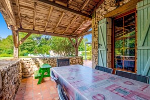 An outdoor patio with a wooden roof, stone walls, and a table set for dining. - Homerez - House in Thenac (Thenac)
