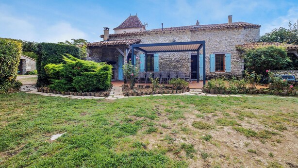 Une maison en pierre avec un toit en tuiles, un patio couvert et un jardin bien entretenu.