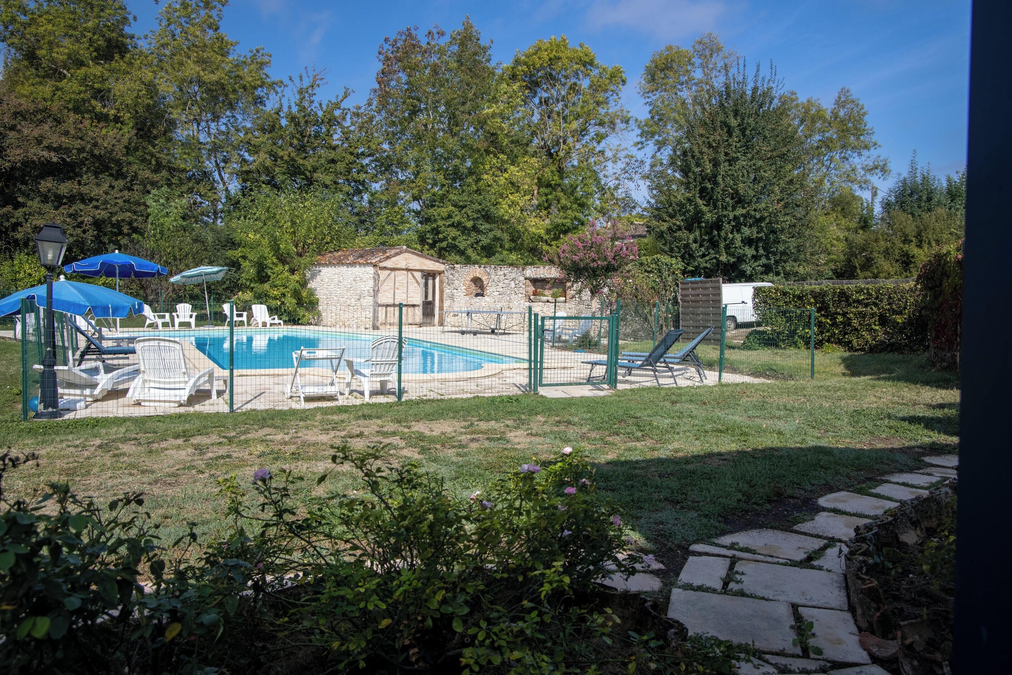 A backyard with a swimming pool, lounge chairs, and a stone building.
